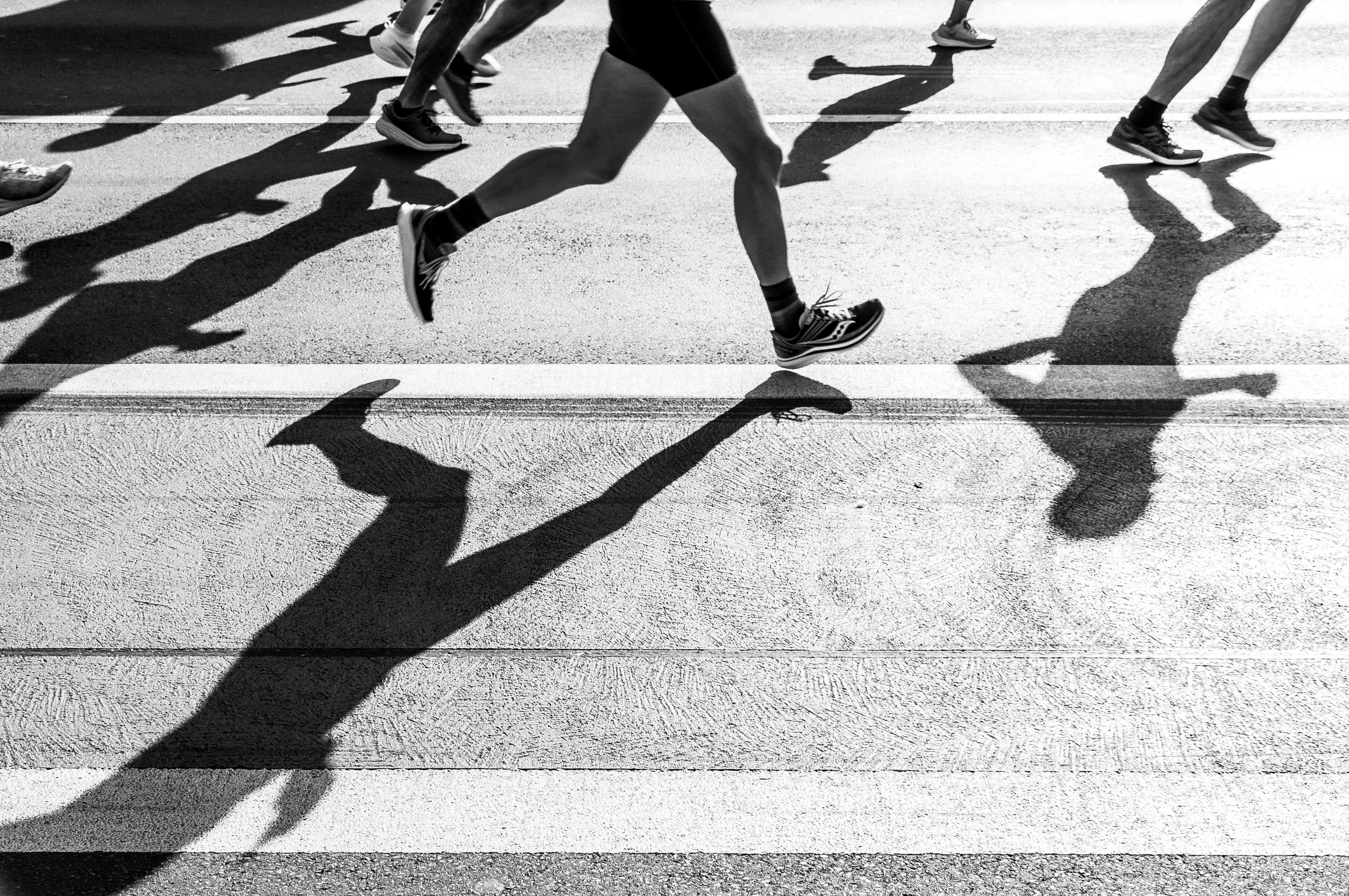 Runners and their shadows moving together along a sunlit road